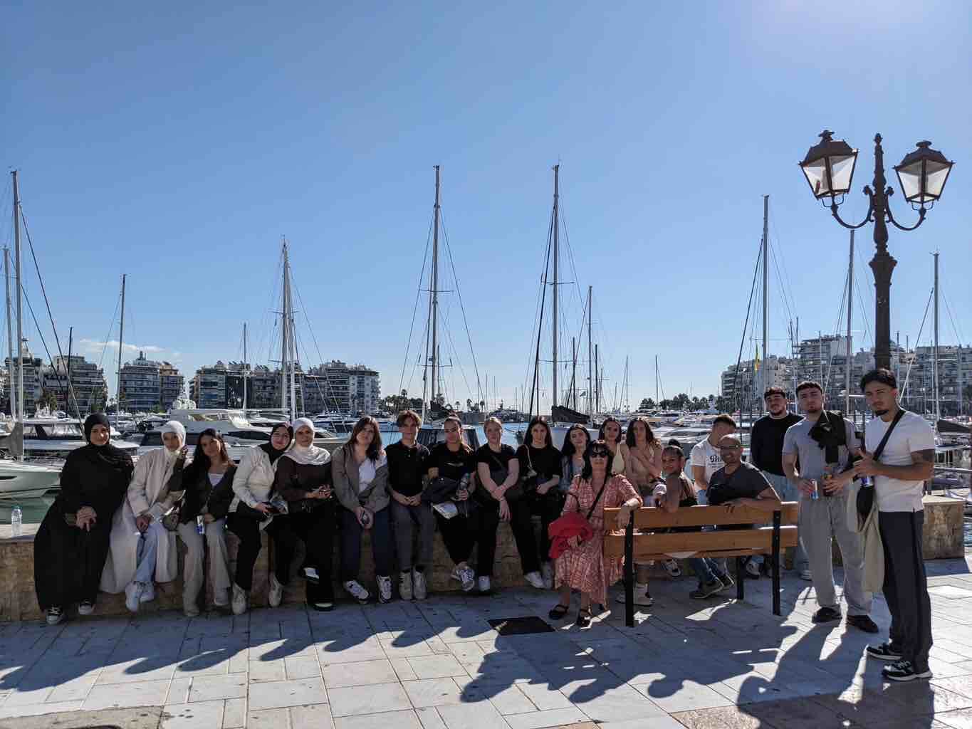 Eine Gruppe von Menschen posiert an einem sonnigen Tag vor einer Reihe von Yachten im Hafen von Athen.