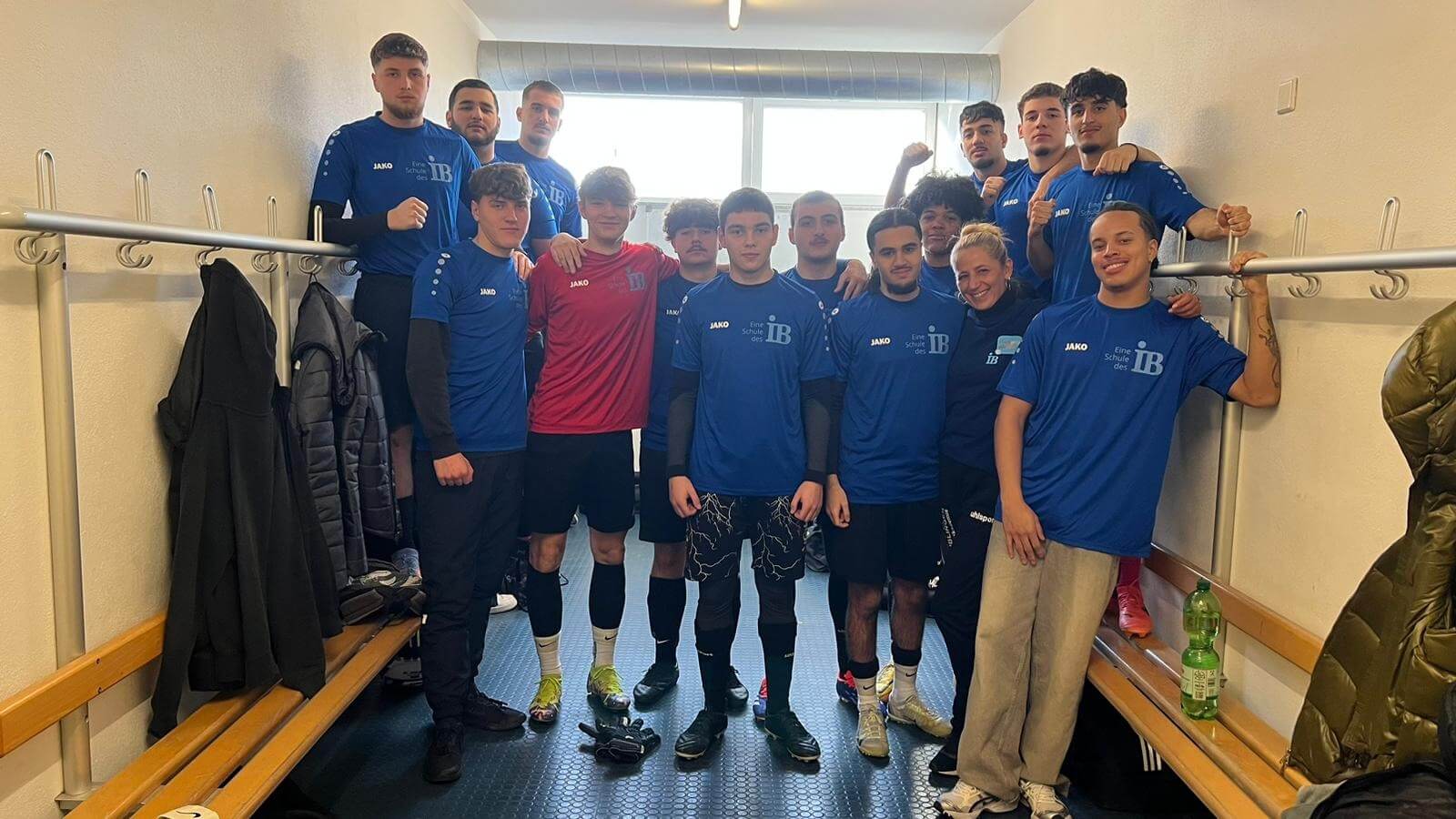 Eine Gruppe junger Fußballspieler posiert in einem Umkleideraum in blauen Trikots für ein Mannschaftsfoto.