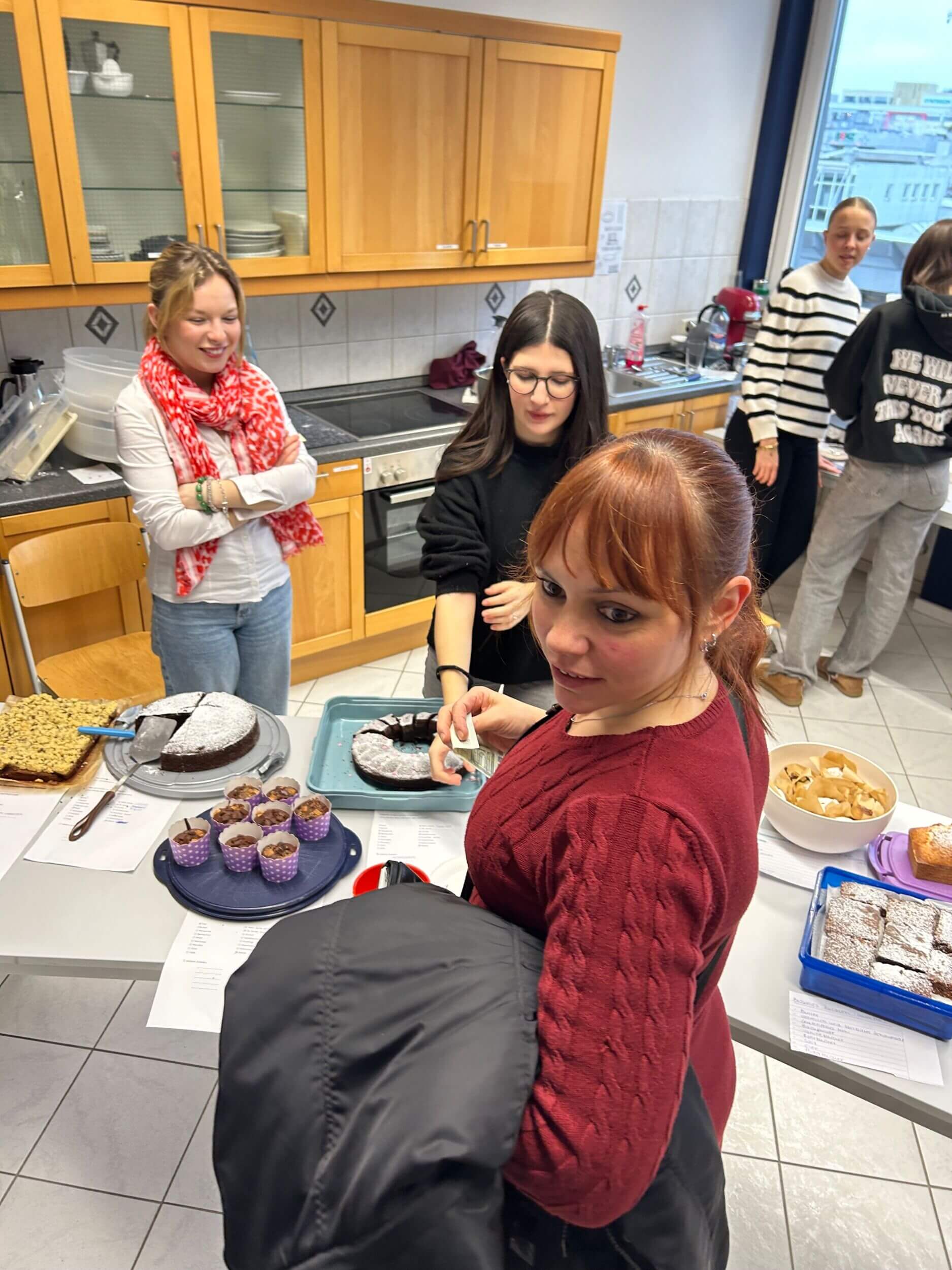In einer Küche genießen mehrere Personen eine Auswahl an Kuchen und Gebäck, während sie sich unterhalten.