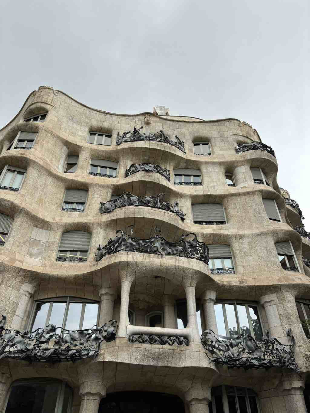 Das Bild zeigt die wellenförmige Fassade eines berühmten Gebäudes in Barcelona unter einem grauen Himmel.