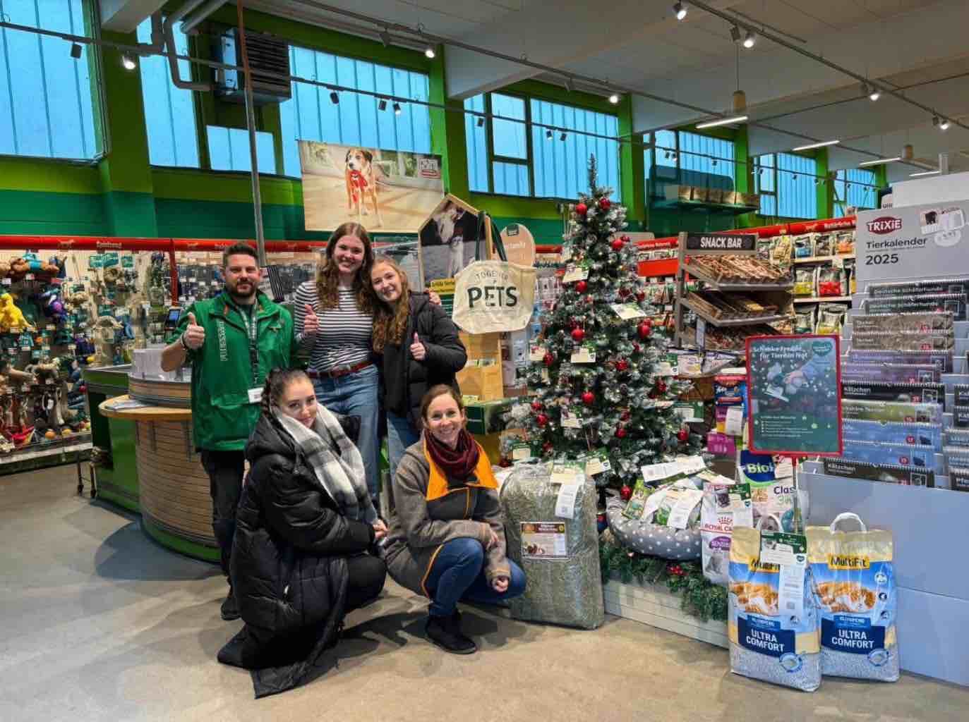 Eine Gruppe von Menschen posiert fröhlich vor einem geschmückten Weihnachtsbaum in einem gut sortierten Tierbedarfsgeschäft.