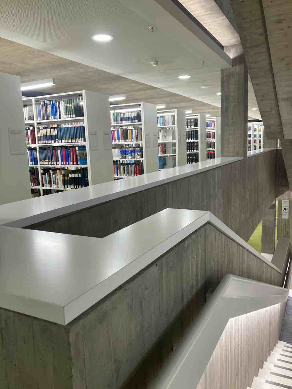 In einer modernen Bibliothek führen Treppen vorbei an gut sortierten Bücherregalen.