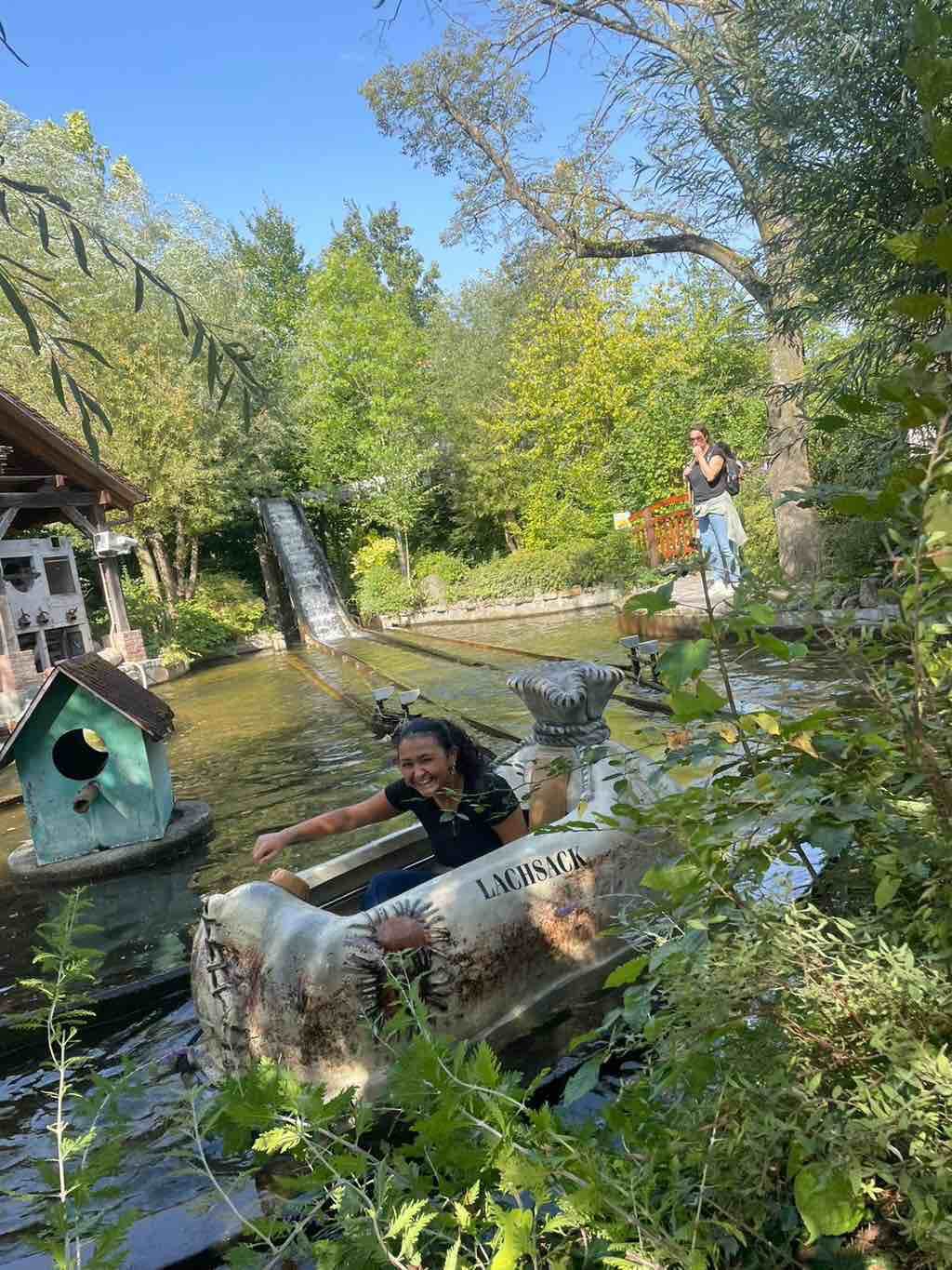 Eine Frau lacht fröhlich in einem Boot auf einem Wasserkanal, während sie eine Wasserattraktion im Grünen genießt.